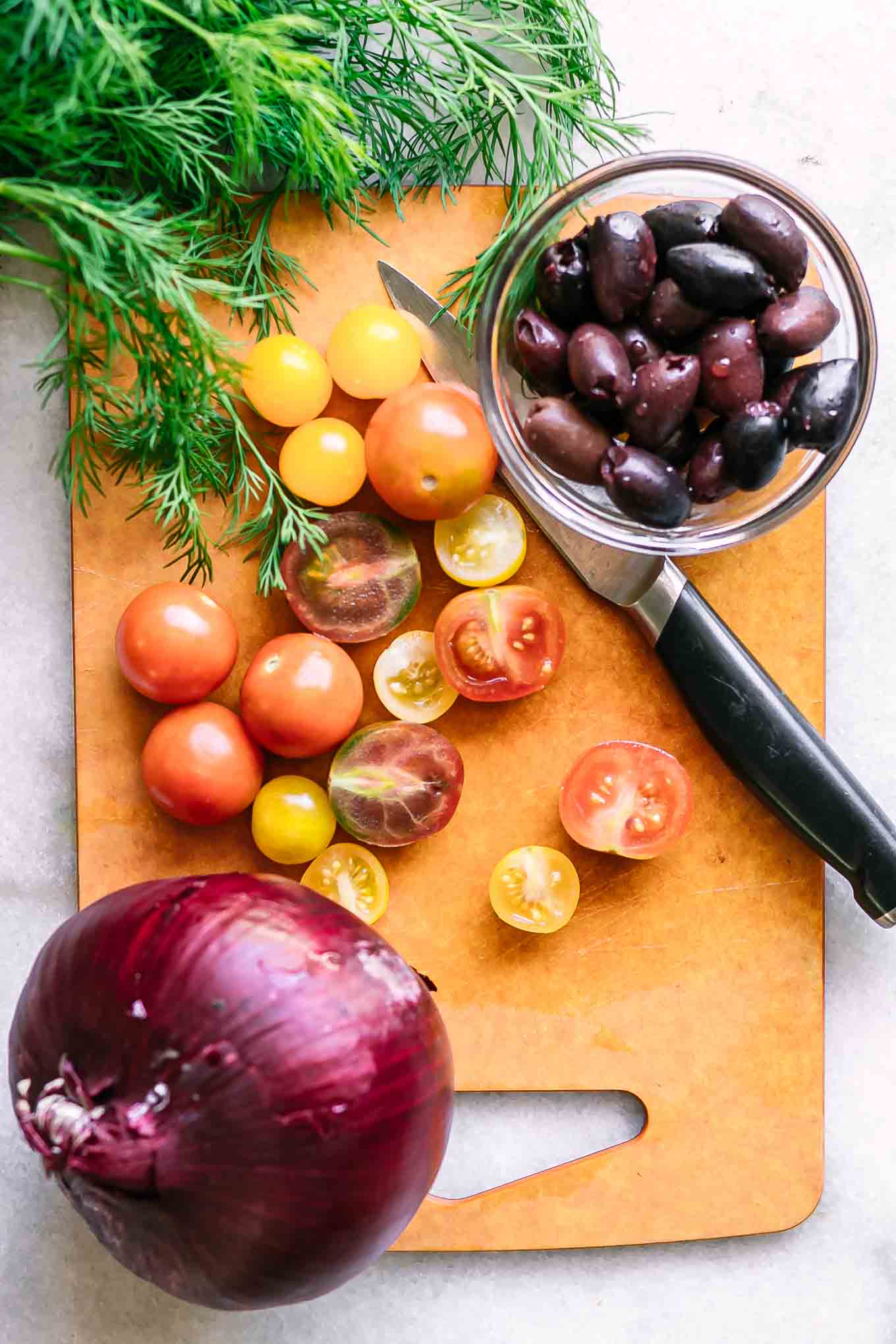 a wood cutting board with sliced tomatoes, onions, and fresh dill