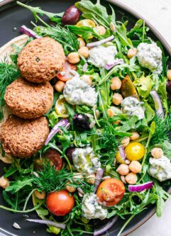 a plate with arugula salad with falafel, red onion, olives, tomatoes, tzatziki, hummus, and sunflower seeds