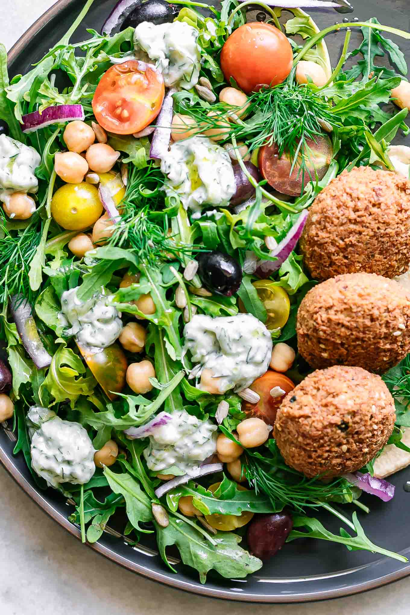 a plate with a salad with arugula, falafel, tzatziki, chickpeas, and hummus