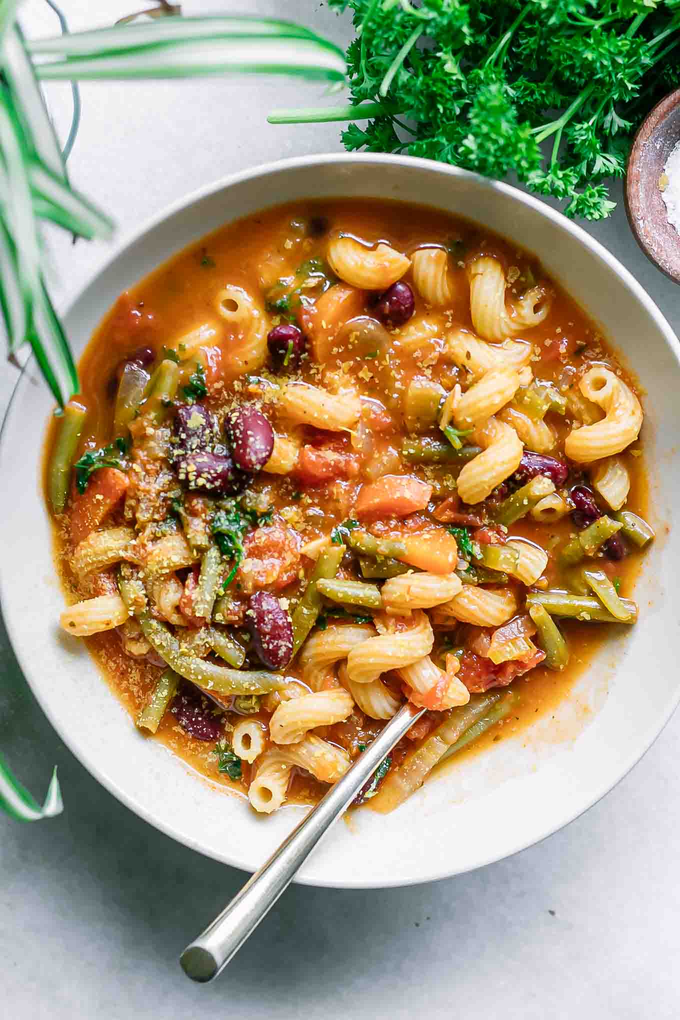 a bowl of vegan minestrone soup on a white table with a gold spoon