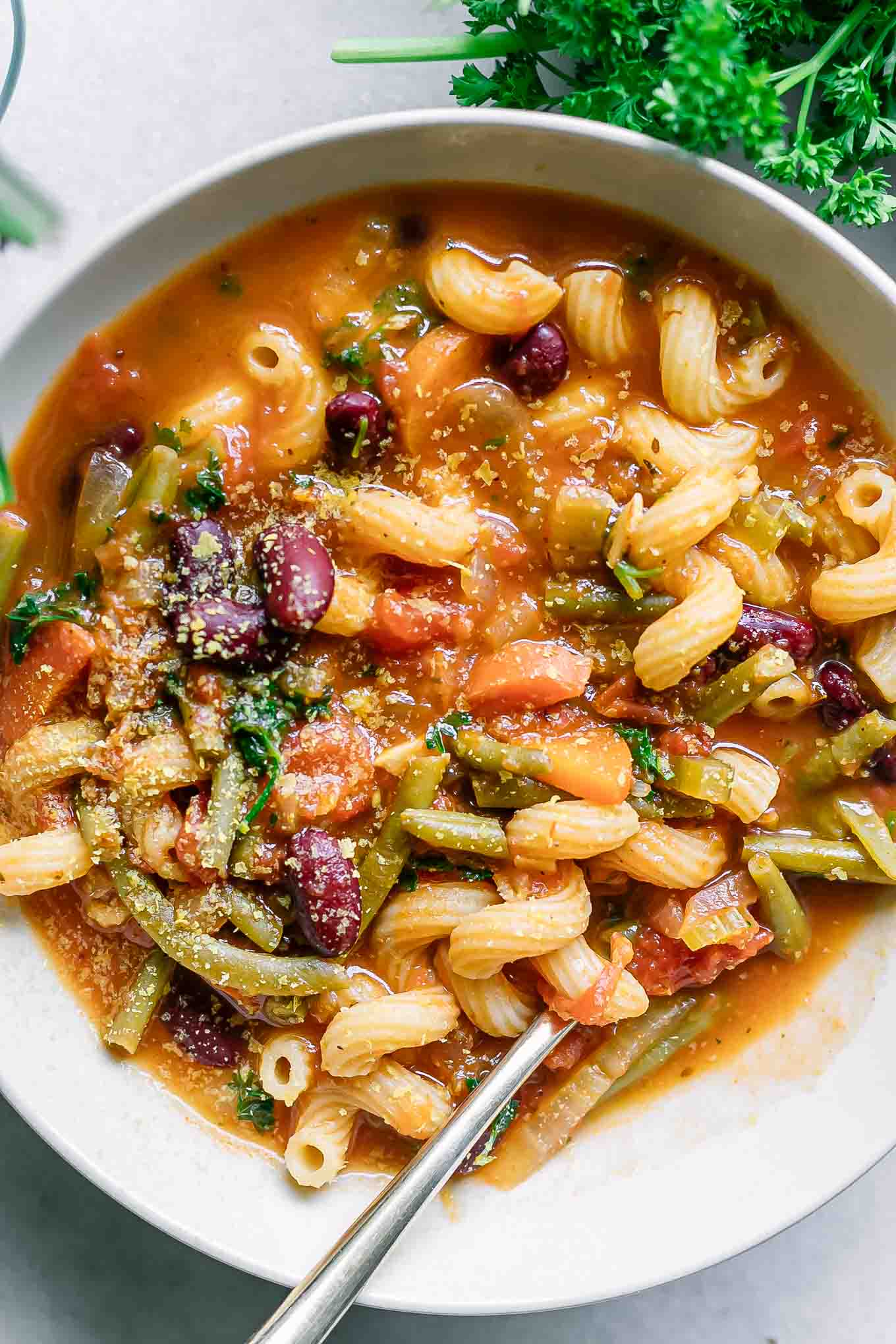 a close up photo of minestrone soup with kidney beans and cavatappi pasta noodles with a gold fork