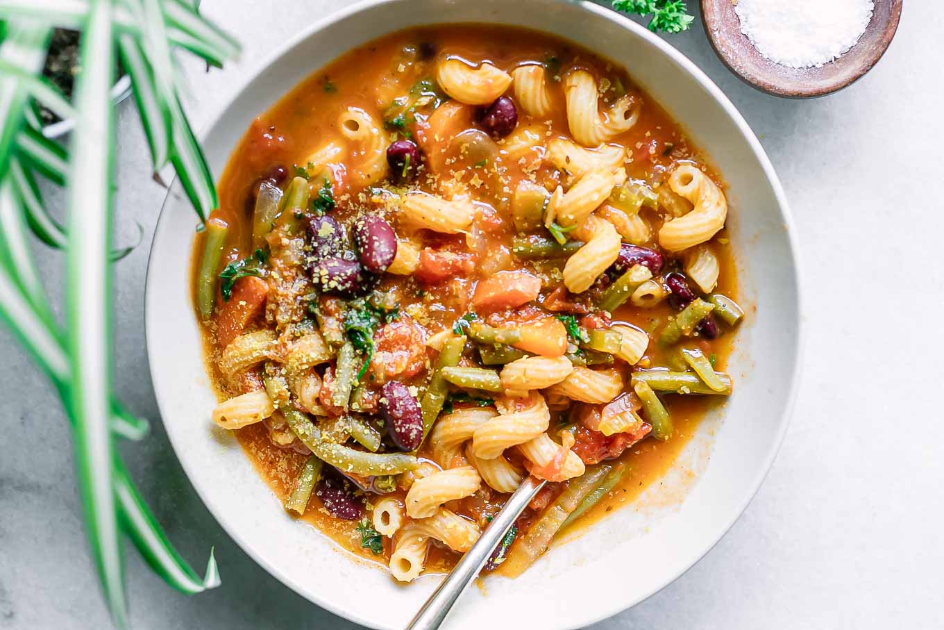 a white bowl of vegan minestrone soup on a white table with a gold fork