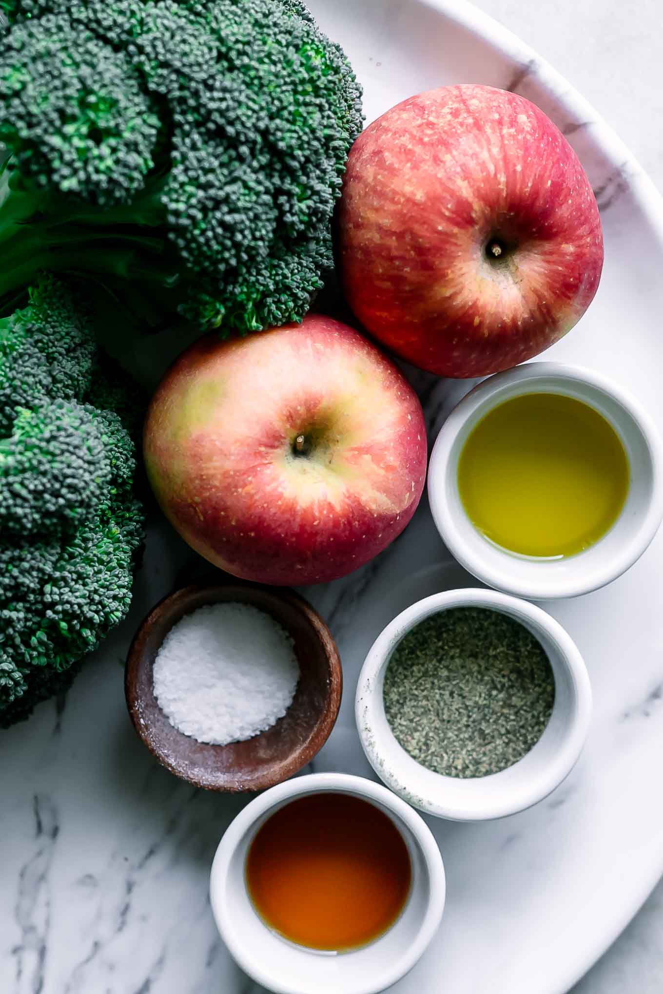 broccoli, apples, oil, maple syrup, cinnamon for roasting on a white table