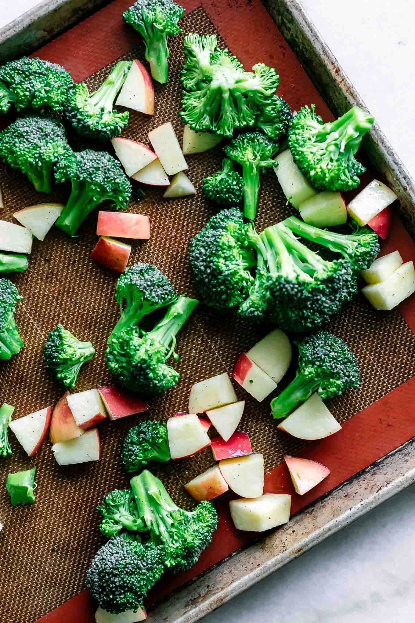 cut broccoli and apples on a baking sheet before roasting