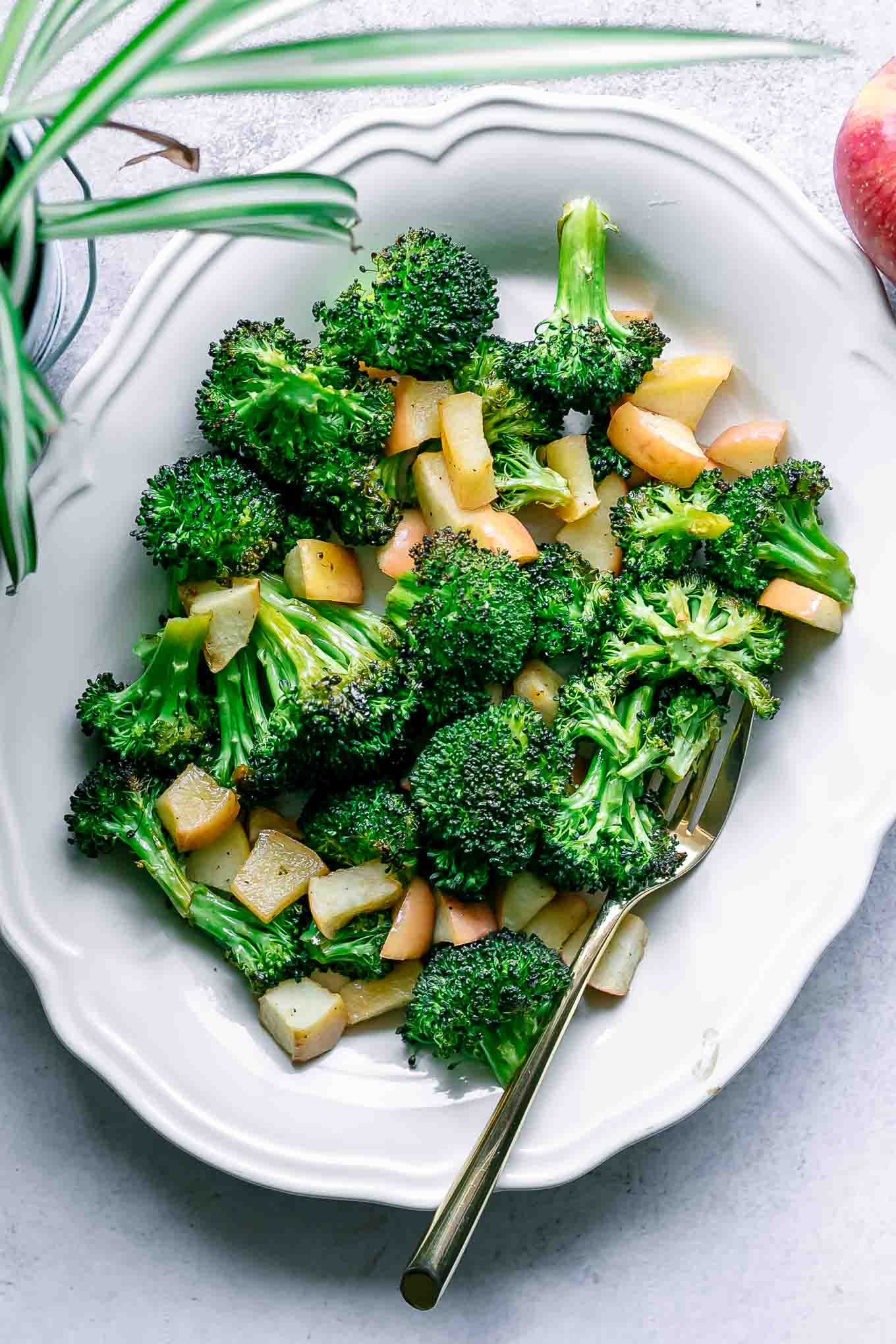 roasted broccoli and apples on a white plate with a gold fork