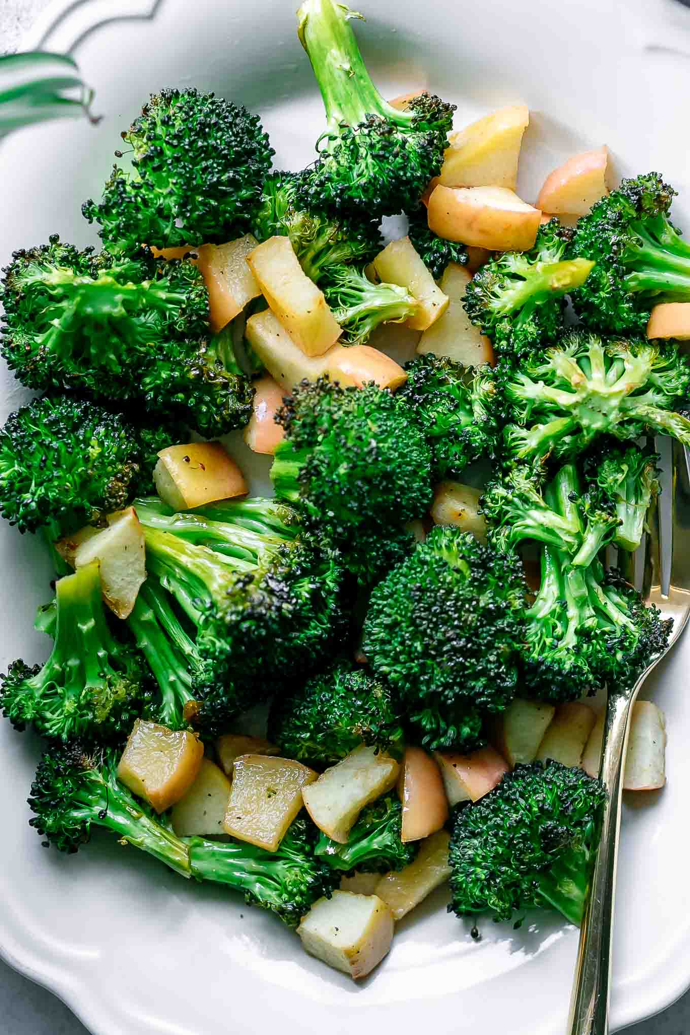 a close up photo of broccoli and apples on a white plate