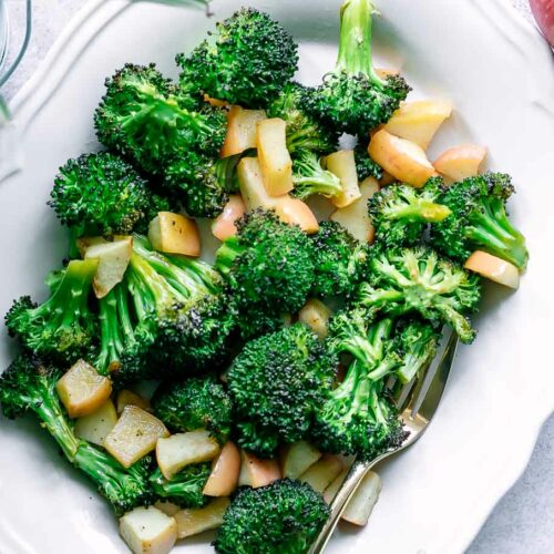 a white plate with baked broccoli and apples side dish on a white table