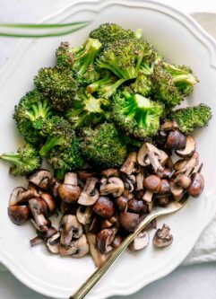a white plate with roasted mushrooms and broccoli with a gold fork