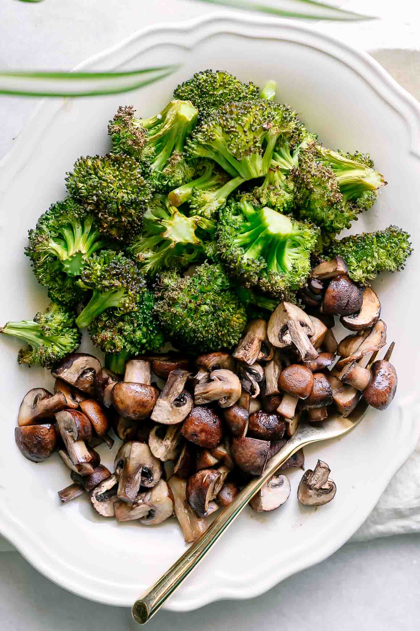 a white plate with roasted mushrooms and broccoli with a gold fork