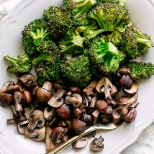 roasted broccoli and mushrooms on a white plate with a gold fork