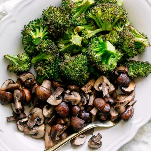 roasted broccoli and mushrooms on a white plate with a gold fork