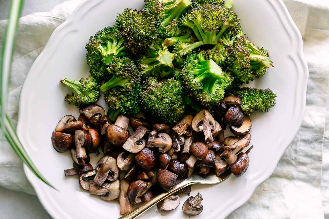 roasted broccoli and mushrooms on a white plate with a gold fork