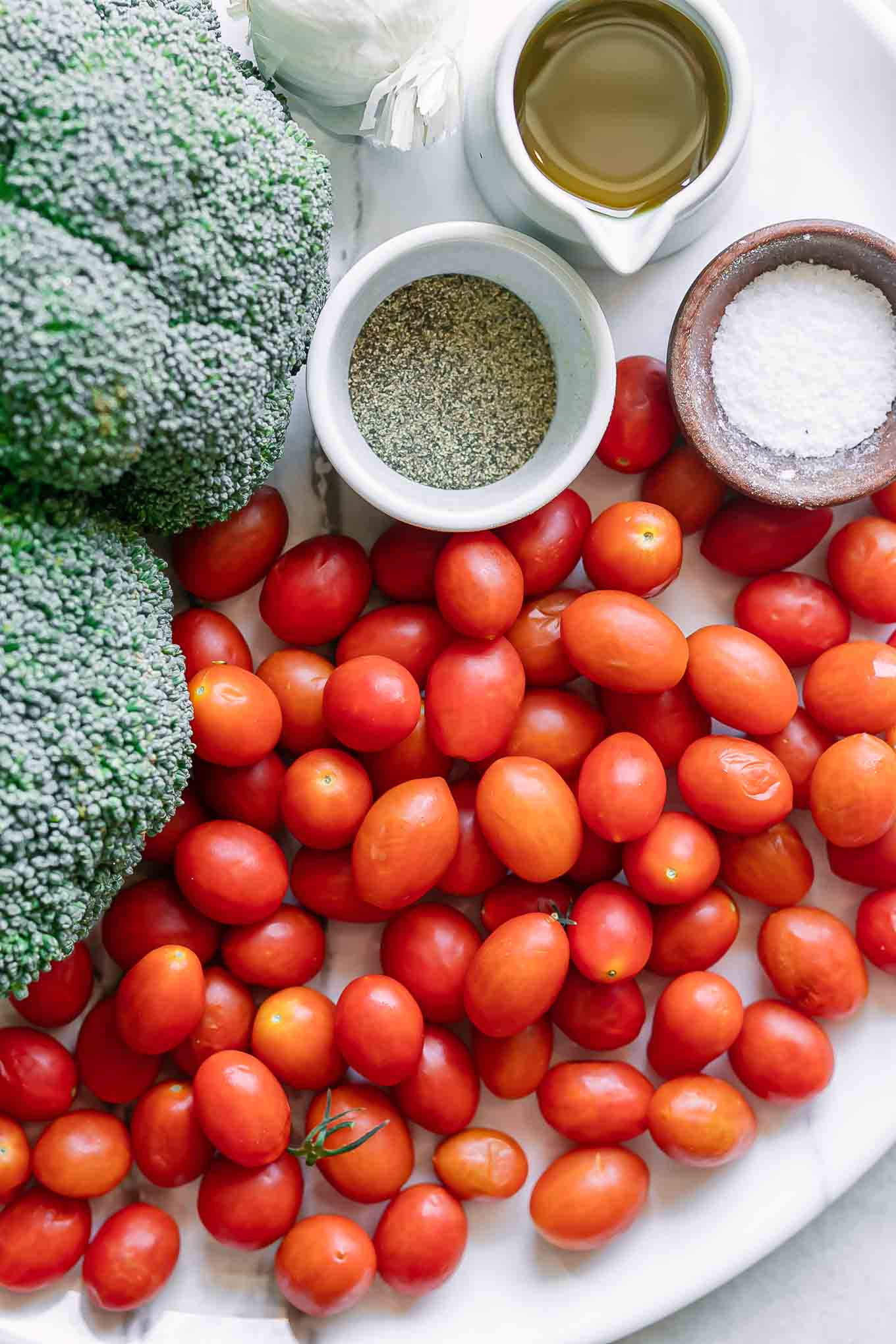 broccoli, cherry tomatoes, onion, oil, salt, and pepper on a table before roasting