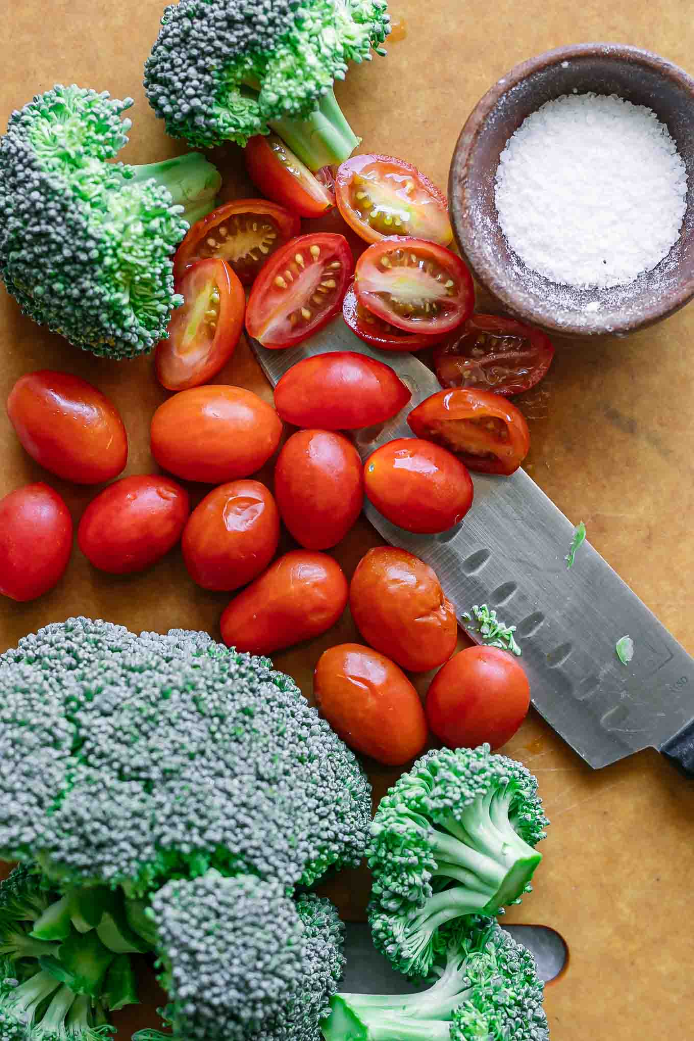 cut tomatoes and broccoli on a wood cutting board with a knife