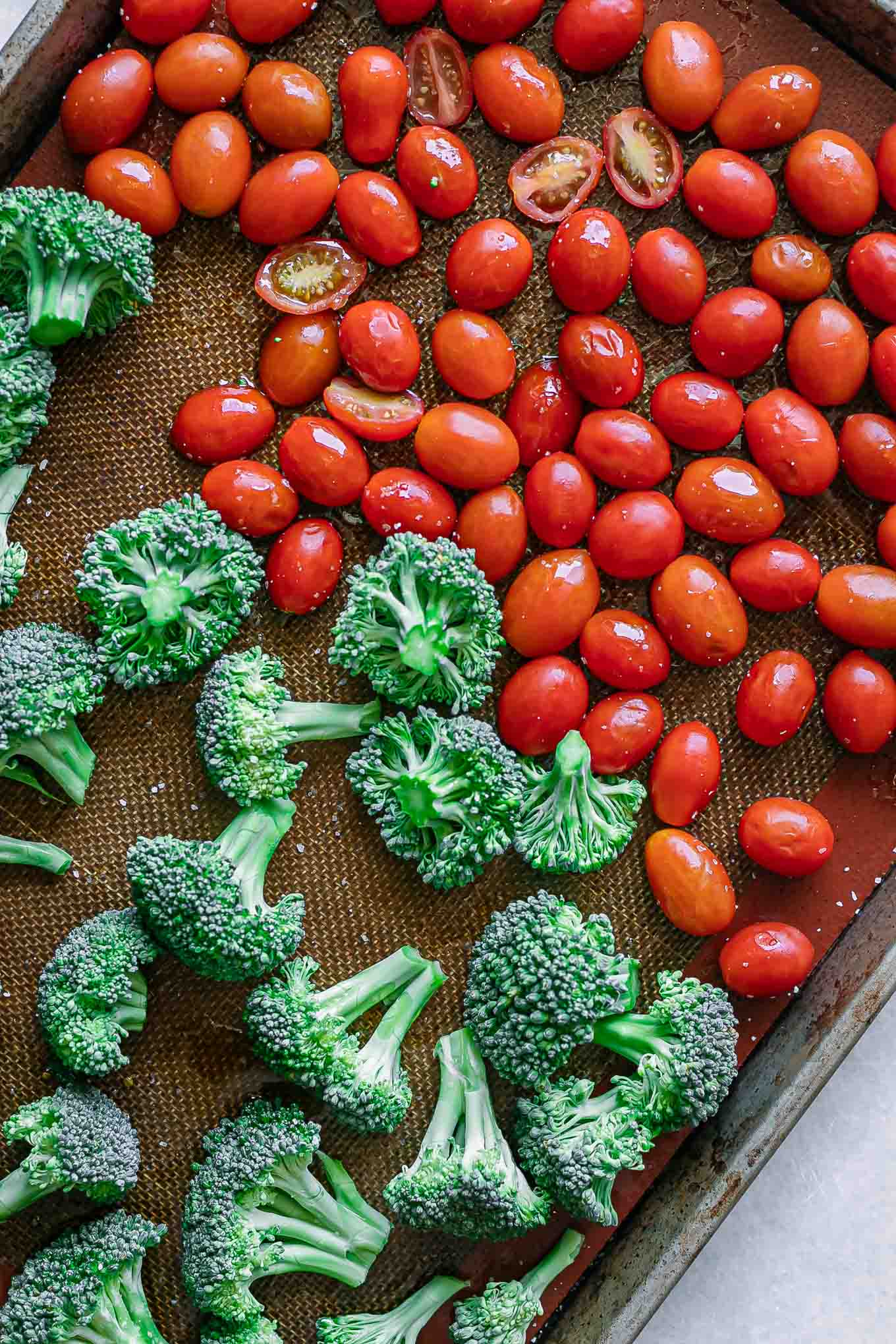 cut broccoli florets and cherry tomatoes on a baking sheet before roasting