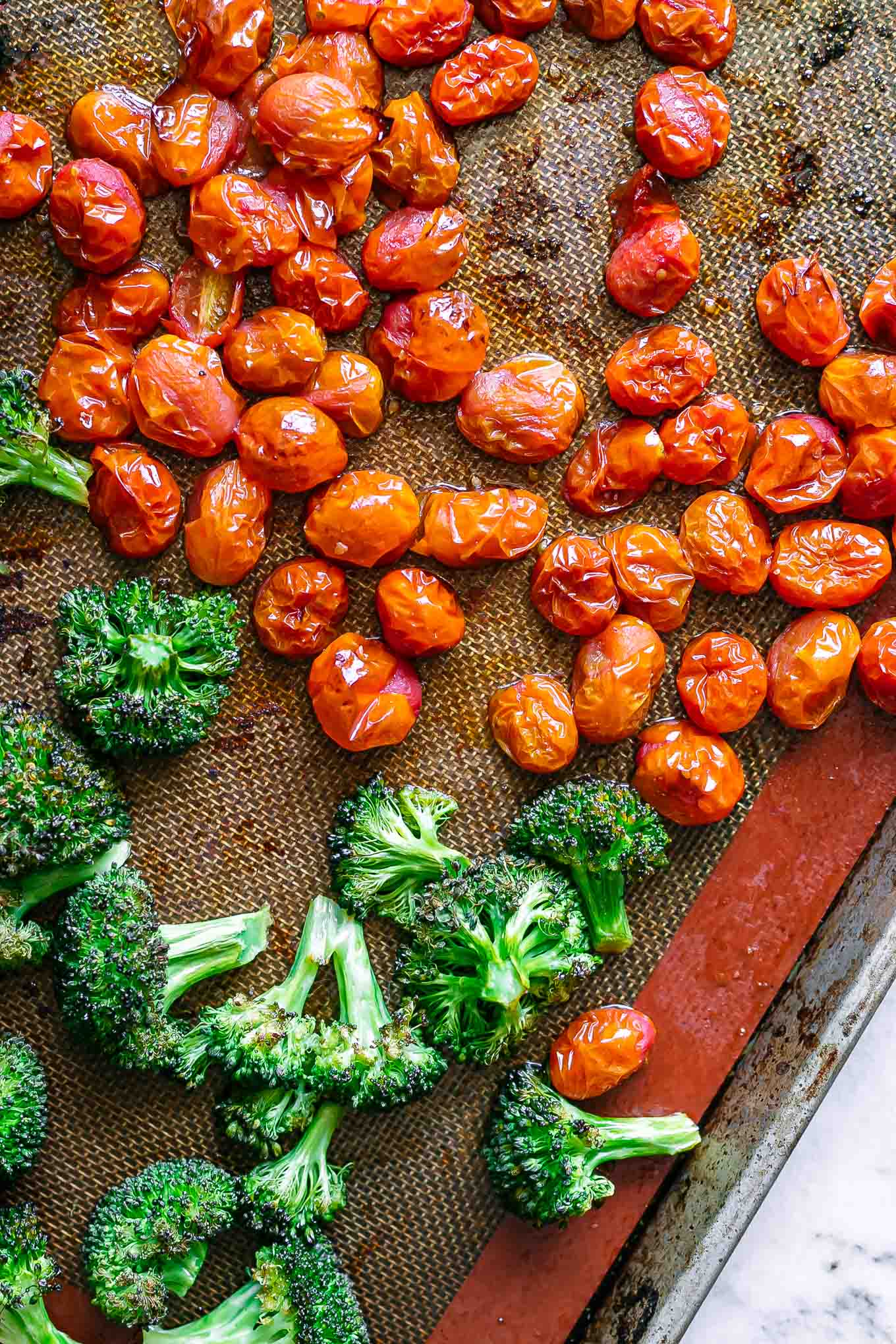 roasted cherry tomatoes and broccoli on a baking sheet after cooking