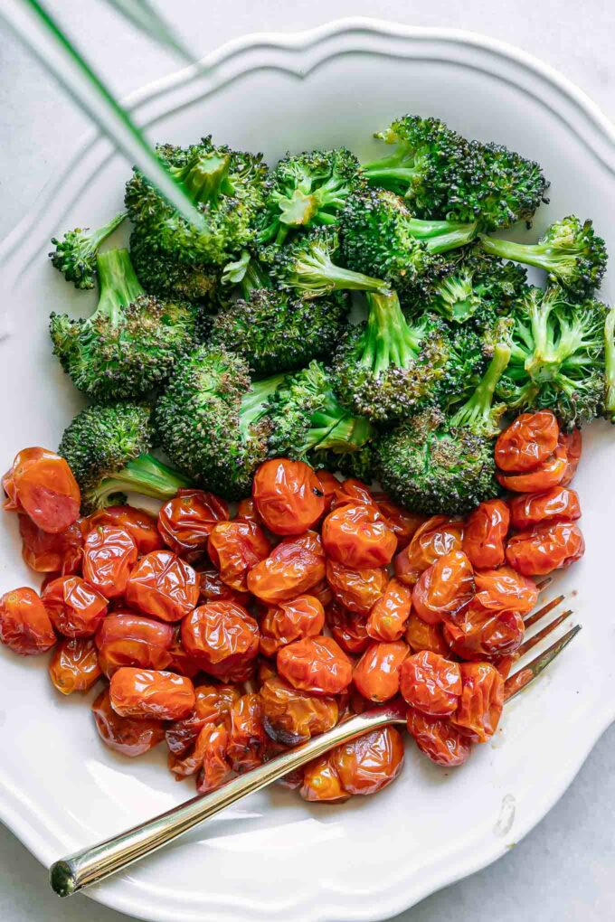 a white plate with roasted broccoli and tomatoes and a gold fork