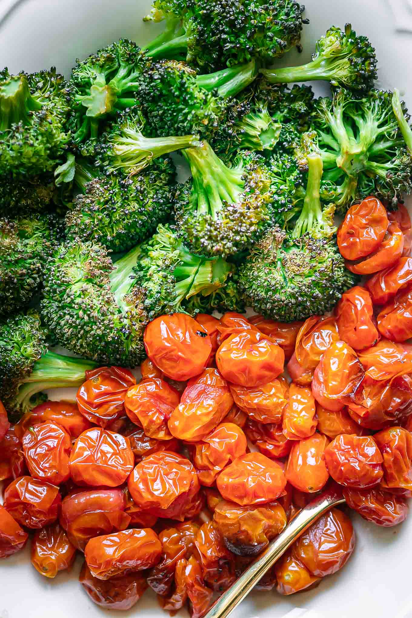 a close up photo of roasted broccoli and cherry tomatoes on a white plate
