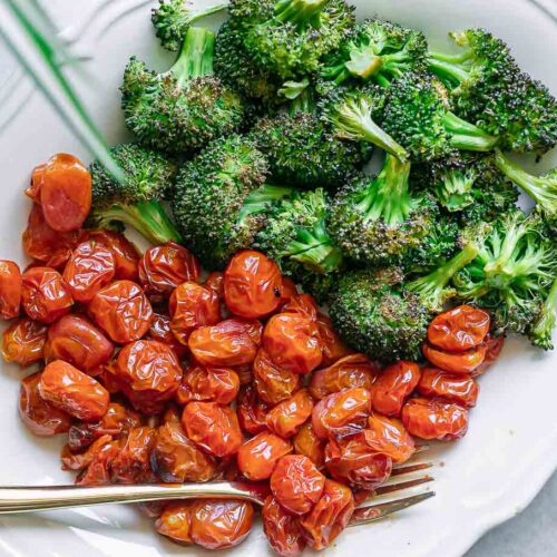 a white plate with roasted broccoli and tomatoes with a gold fork
