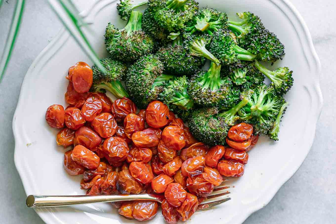 a white plate with roasted broccoli and tomatoes with a gold fork