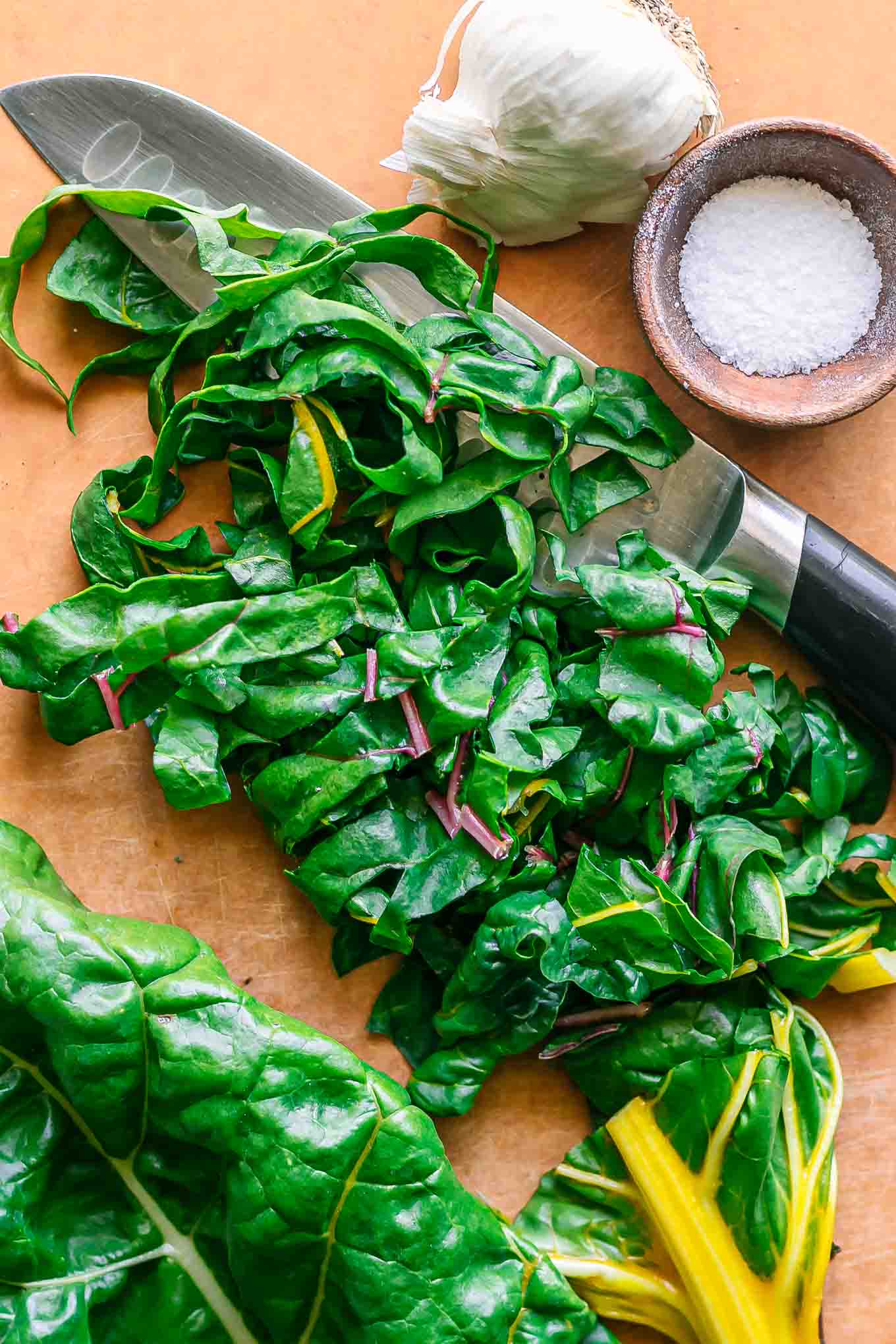 cut swiss chard leaves on a wood cutting board with a knife