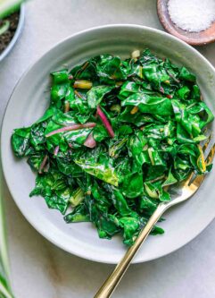 a plate with pan fried chard leaves on a plate with a gold fork