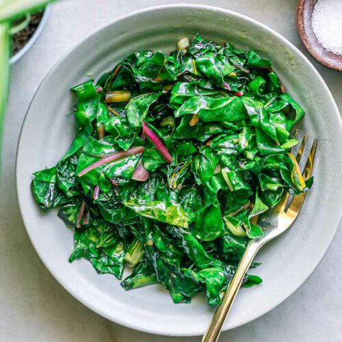 sauteed swiss chard leaves on a plate with a gold fork