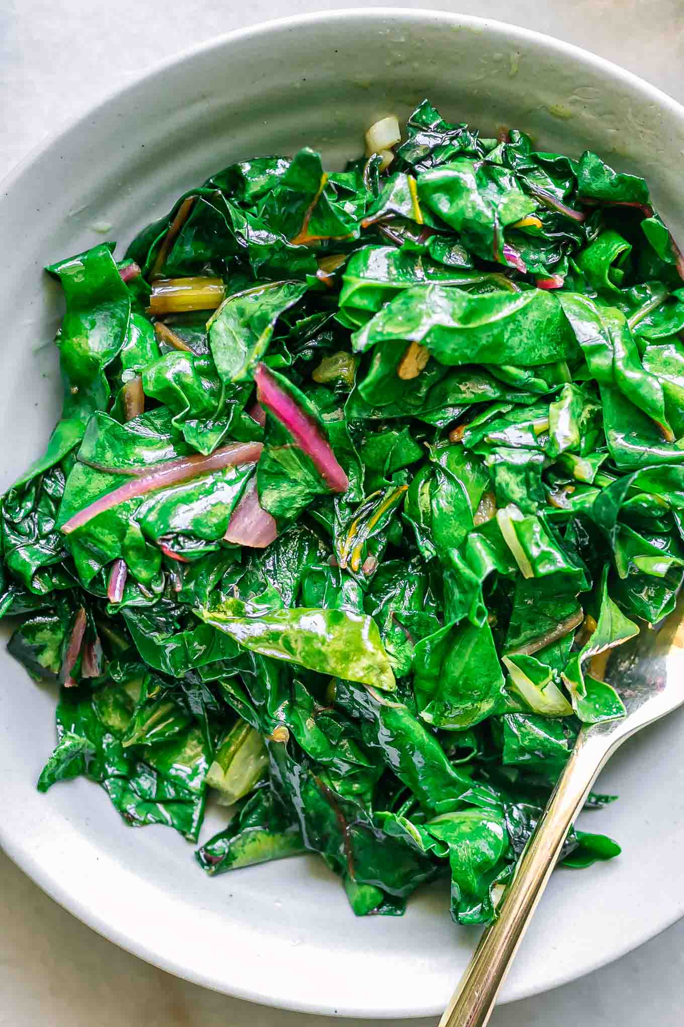 a close up photo of sauteed chard leaves on a white plate with a gold fork