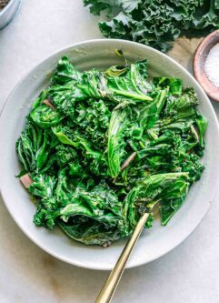a bowl of pan fried chard and kale with a gold fork on a white table