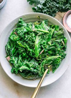 a bowl of pan fried chard and kale with a gold fork on a white table