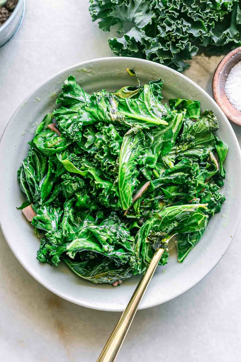 a bowl of pan fried chard and kale with a gold fork on a white table