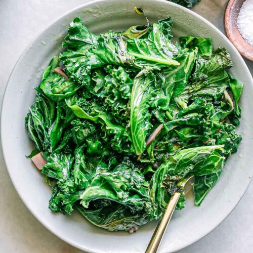 a white bowl with sautéed kale and chard leaves on a white table