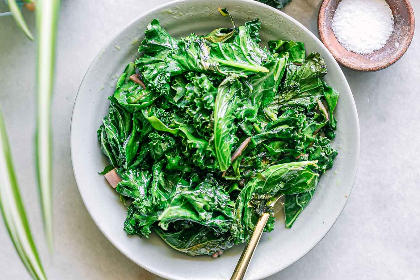 a white bowl with sautéed kale and chard leaves on a white table