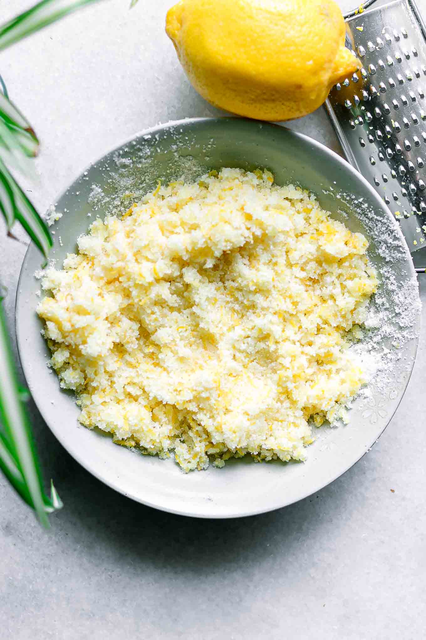 lemon zest and granulated sugar in a bowl on a white table with a lemon