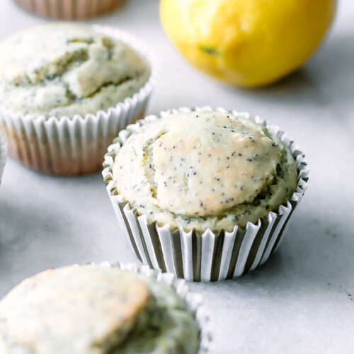 vegan lemon poppyseed muffins on a white table with fresh lemons
