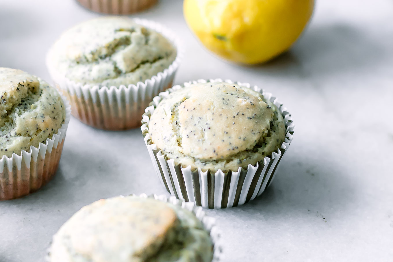 vegan lemon poppyseed muffins on a white table with fresh lemons