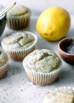 plant-based lemon poppyseed muffins on a white table with a lemon