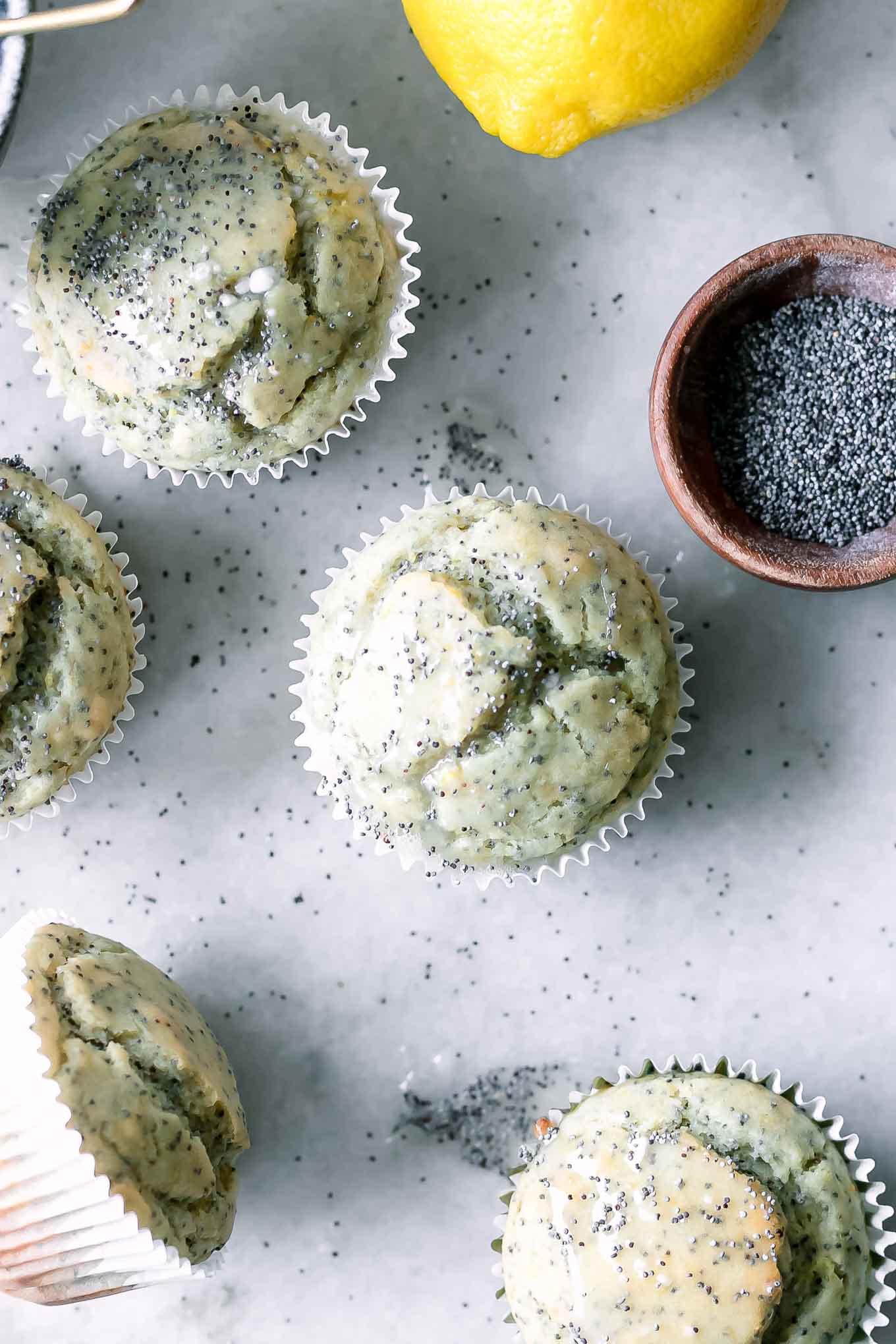 a lemon poppyseed muffin on a white table with a bowl of poppyseeds