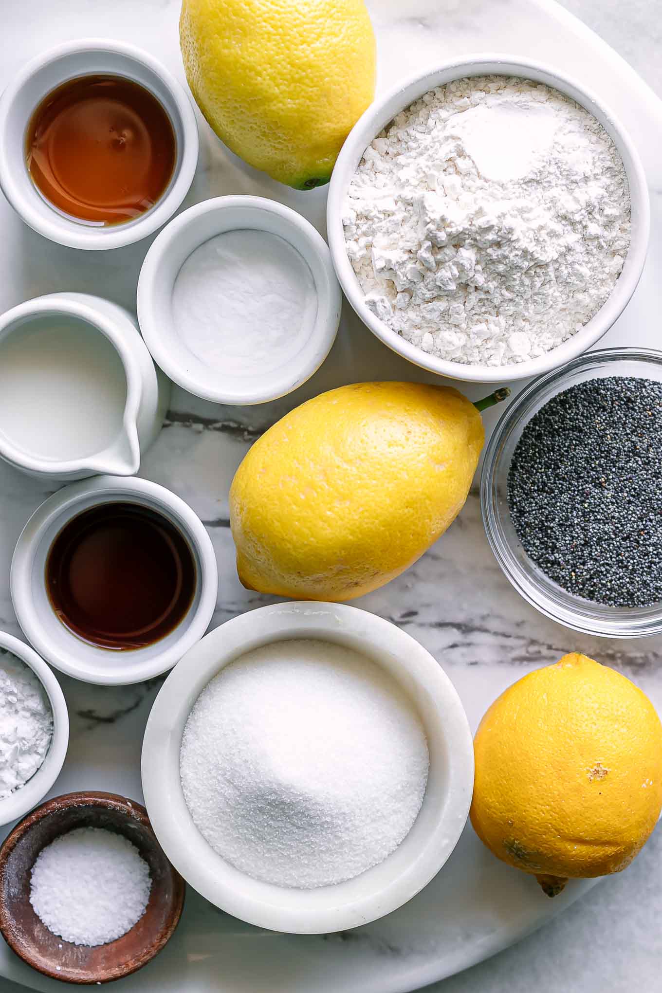 bowls of flour, sugar, lemons, poppyseeds, and other ingredients for pancakes on a white table
