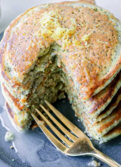 a blue plate with a stack of vegan lemon poppyseed pancakes with a gold fork and a whole lemon