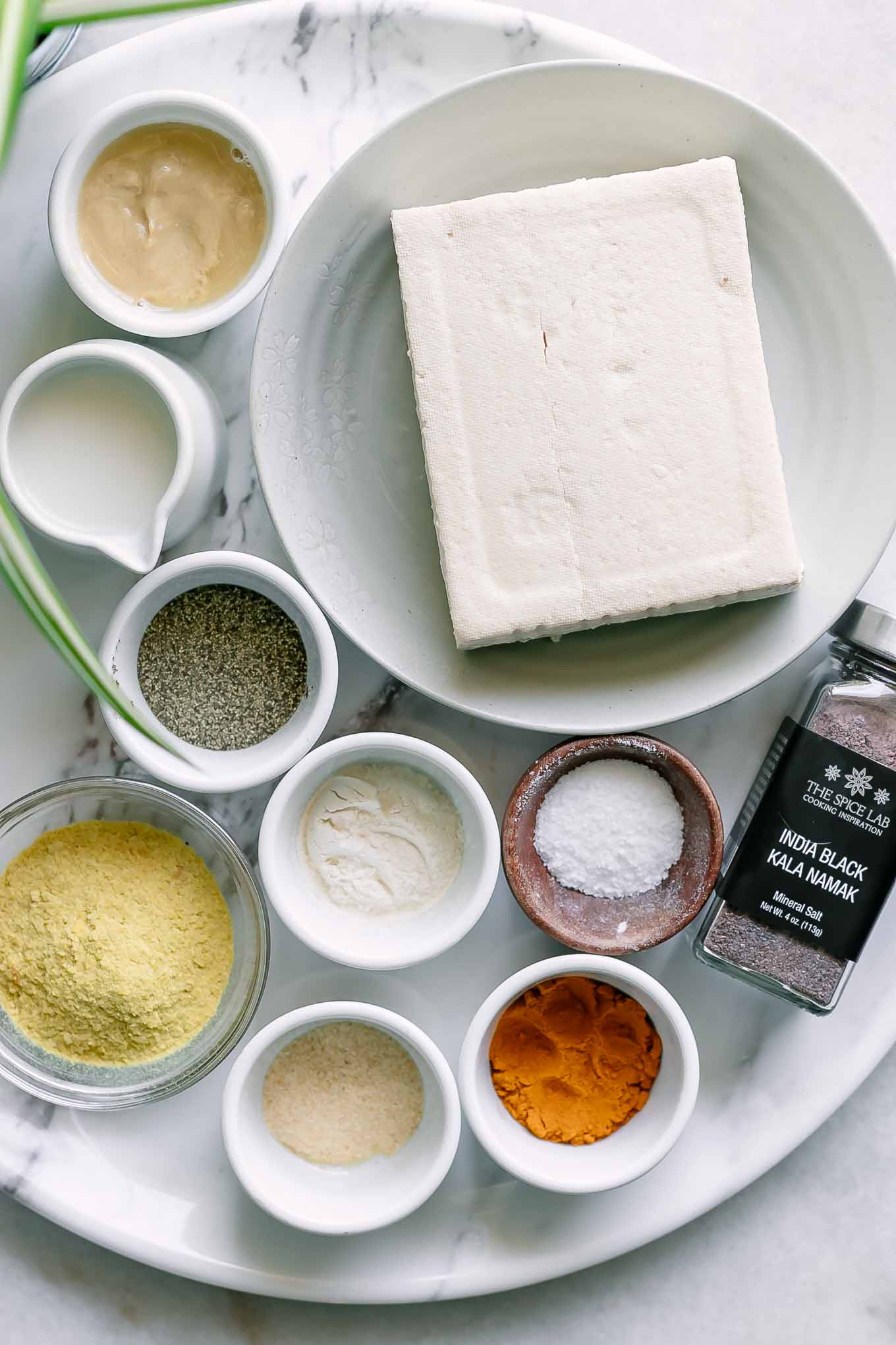 tofu and seasoning ingredients in bowls on a white table for a vegan tofu scramble