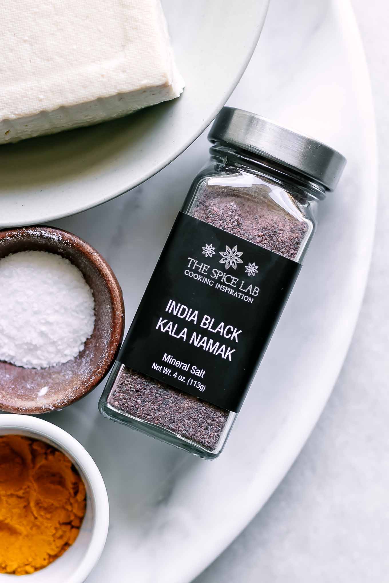 a close up photo of a jar of kala namak black salt on a white table