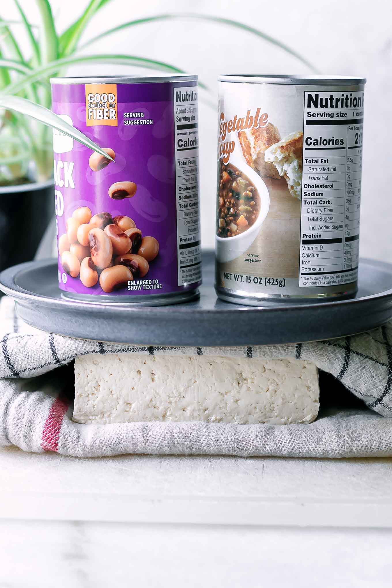 a block of tofu pressing between two kitchen towels with a blue plate with two cans of beans on top