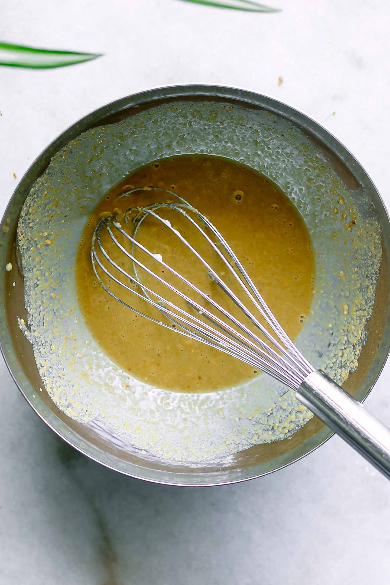 a metal bowl with yellow egg-flavored sauce and a metal whisk for a tofu scramble