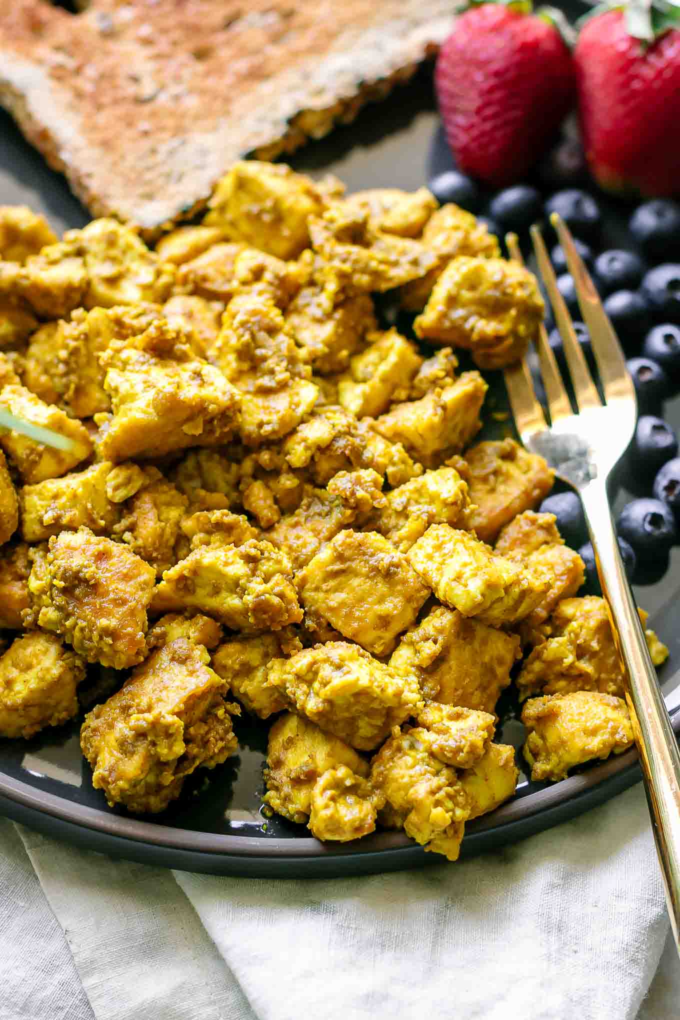 a close up photo of a vegan tofu scramble on a plate with bread and fruit