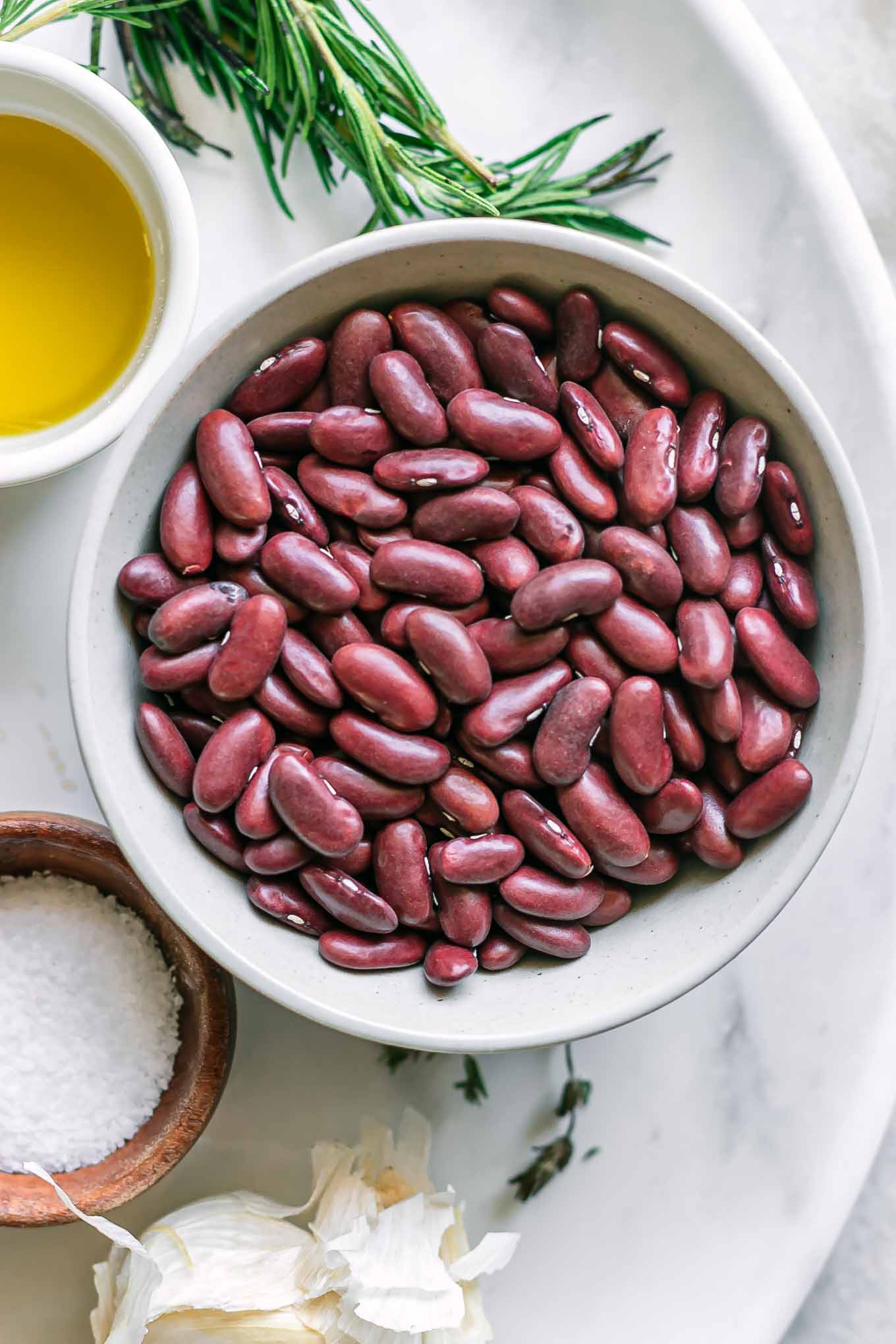bowls of dried kidney beans, oil, salt, garlic, and herbs on a table for cooking in the instant pot