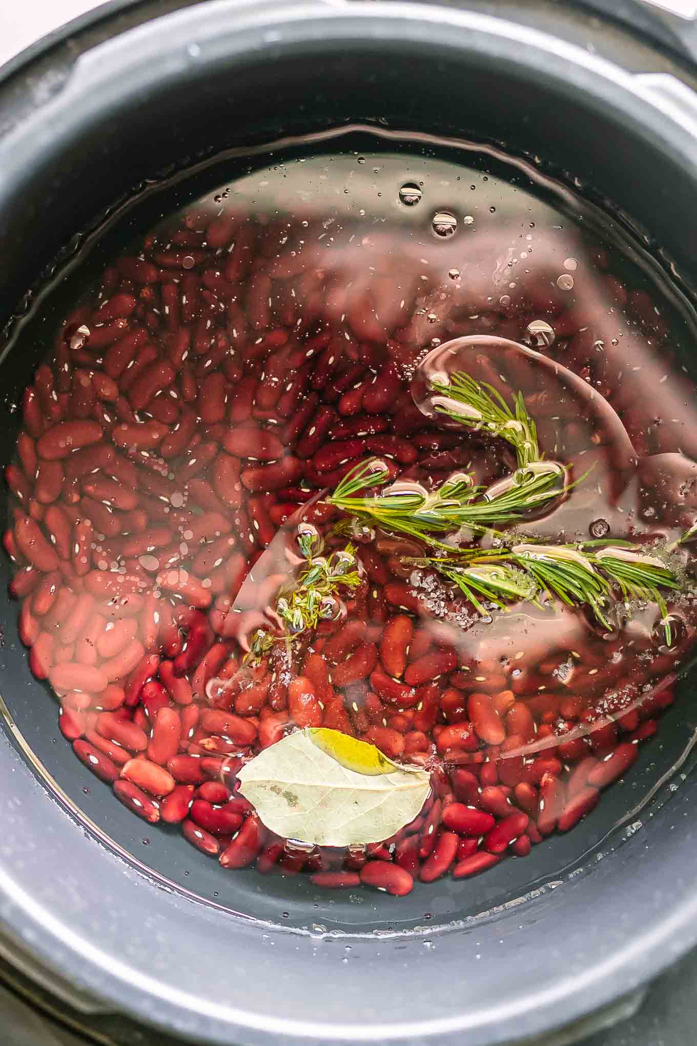 kidney beans in water inside a pressure cooker with herbs