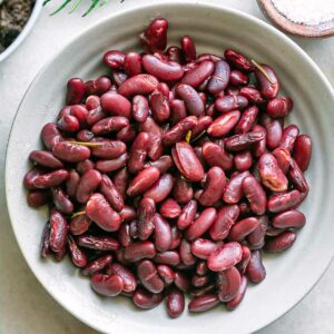 a bowl of cooked kidney beans on a white table with herbs and a bowl of salt