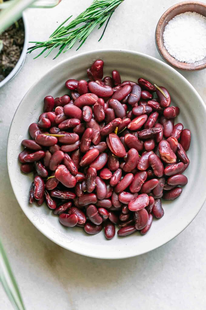 a bowl of cooked kidney beans on a white table with herbs and bowls of seasonings