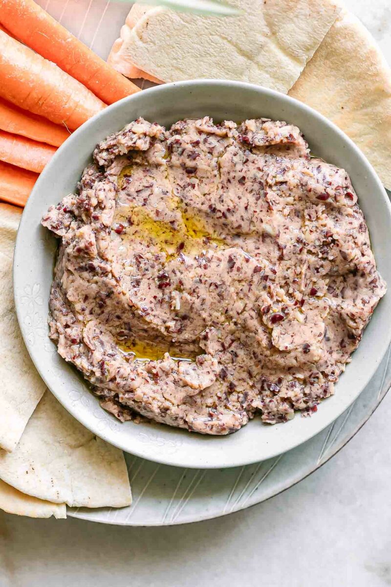 a bowl of kidney bean hummus on a plate with pita bread and carrot sticks